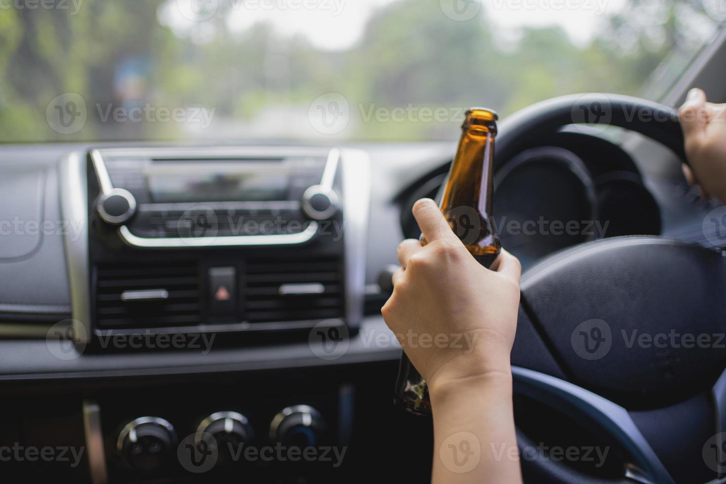 uma mulher sem rosto está bebendo uma garrafa de cerveja enquanto dirige um carro. conceito de dirigir embriagado foto
