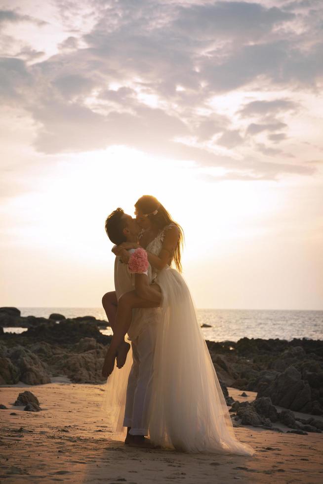 jovem casal abraçado está comemorando seu casamento na praia foto