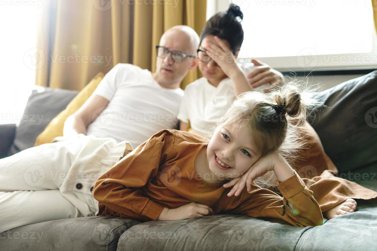 menina feliz assistindo desenhos animados com seus pais cansados foto