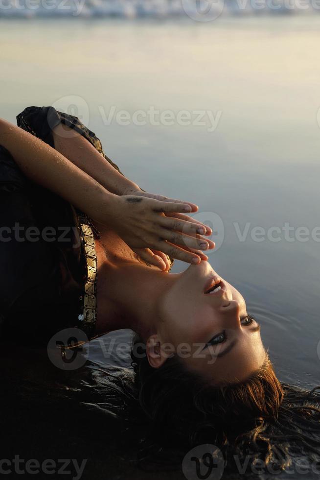 mulher sexy vestindo túnica preta está posando na praia com areia preta foto