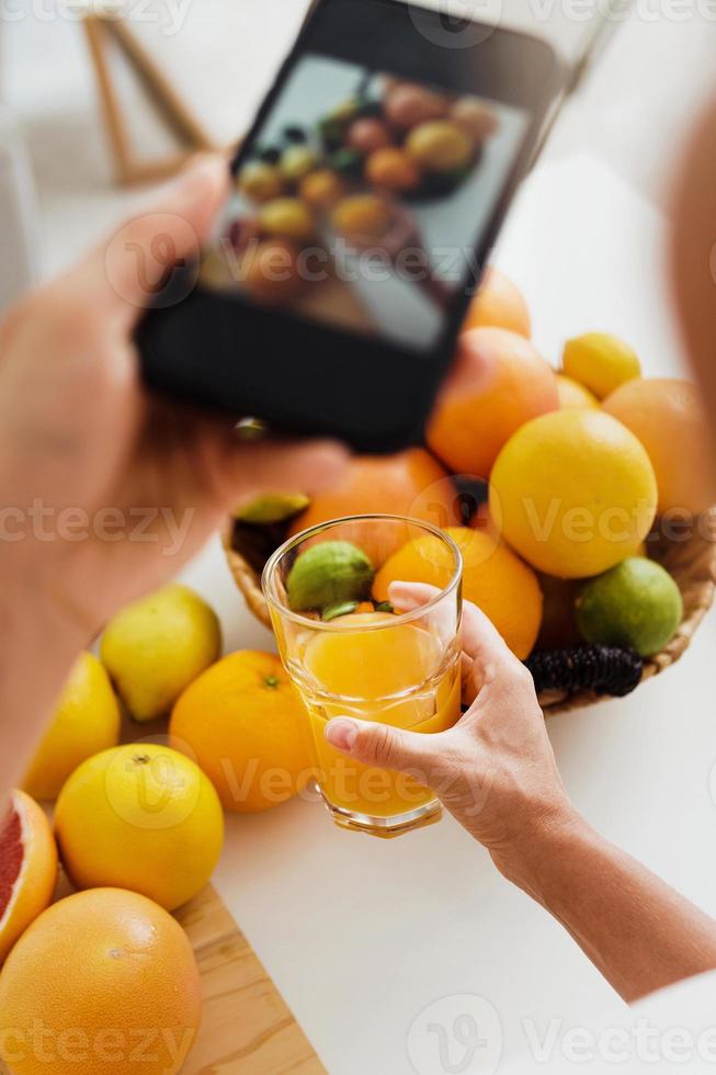 mão feminina com um smartphone tirando fotos de vidro com suco de laranja