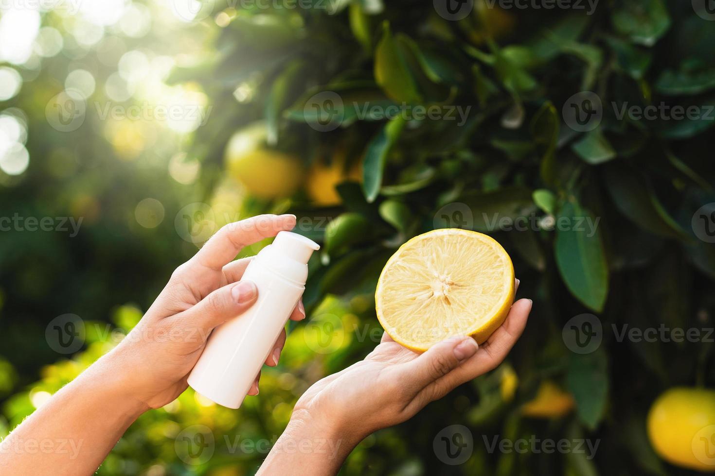mulher segura garrafa de produto para a pele e metade de limão nas mãos no fundo da árvore de limão. foto