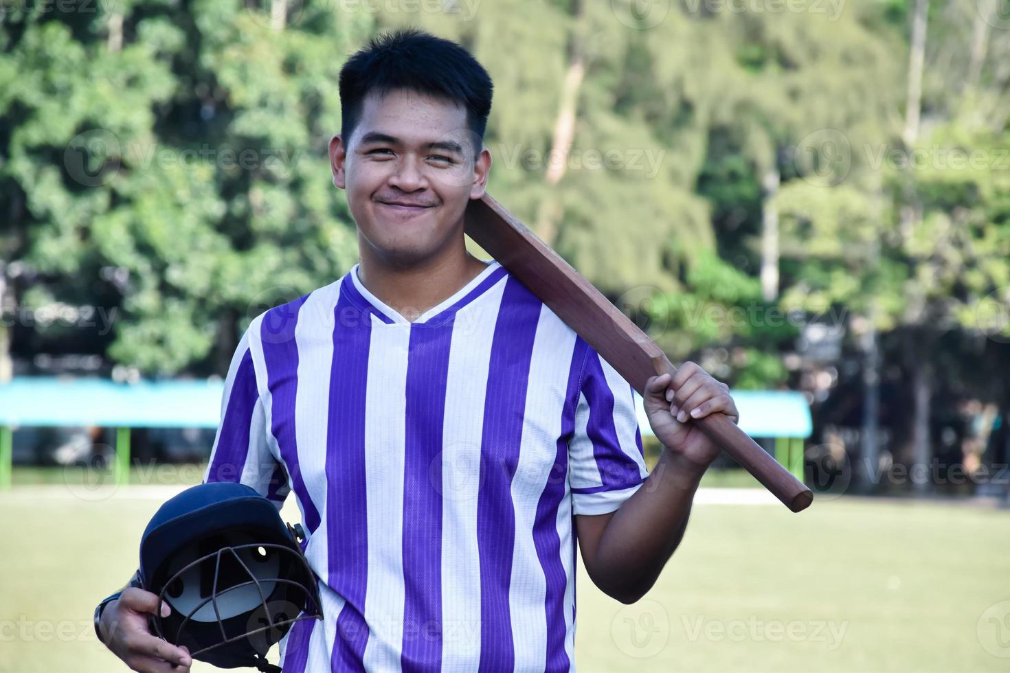 o treinador de críquete masculino segura o capacete e o bastão na quadra de grama verde da escola antes de ensinar o esporte de críquete aos alunos da escola à tarde. foto