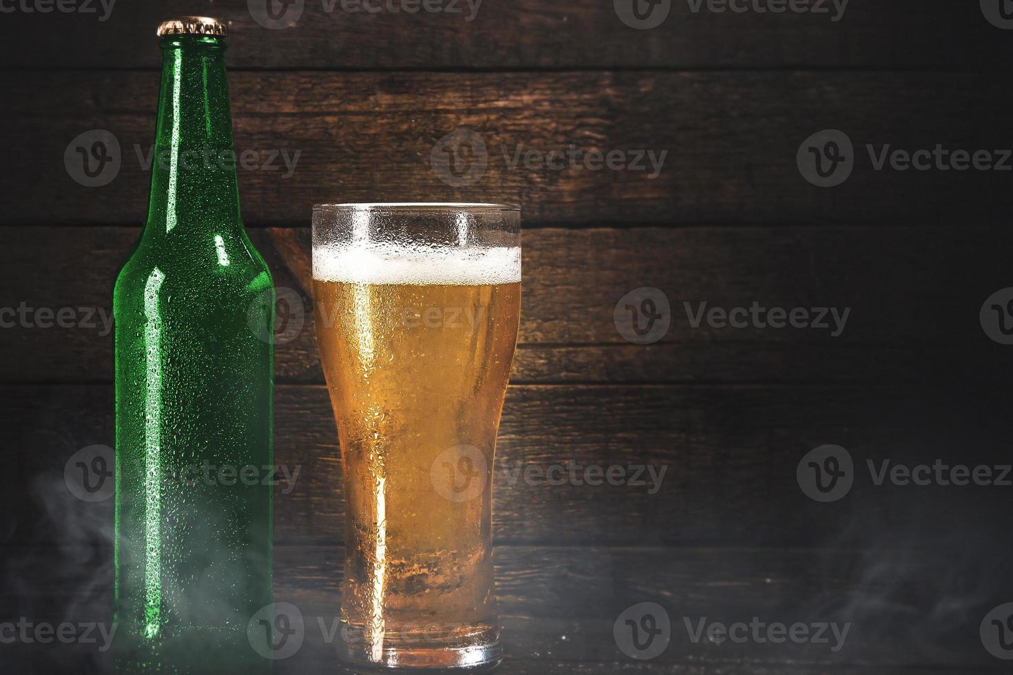 garrafa verde e copo de cerveja pálida sobre fundo de madeira foto