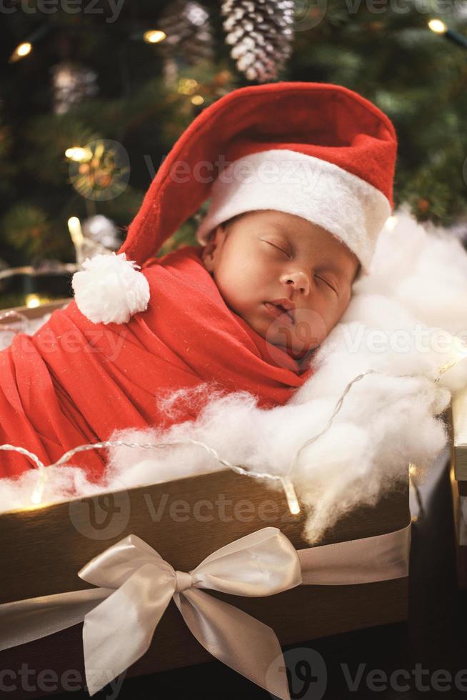 lindo bebê recém-nascido usando chapéu de papai noel está dormindo na caixa de presente de natal foto