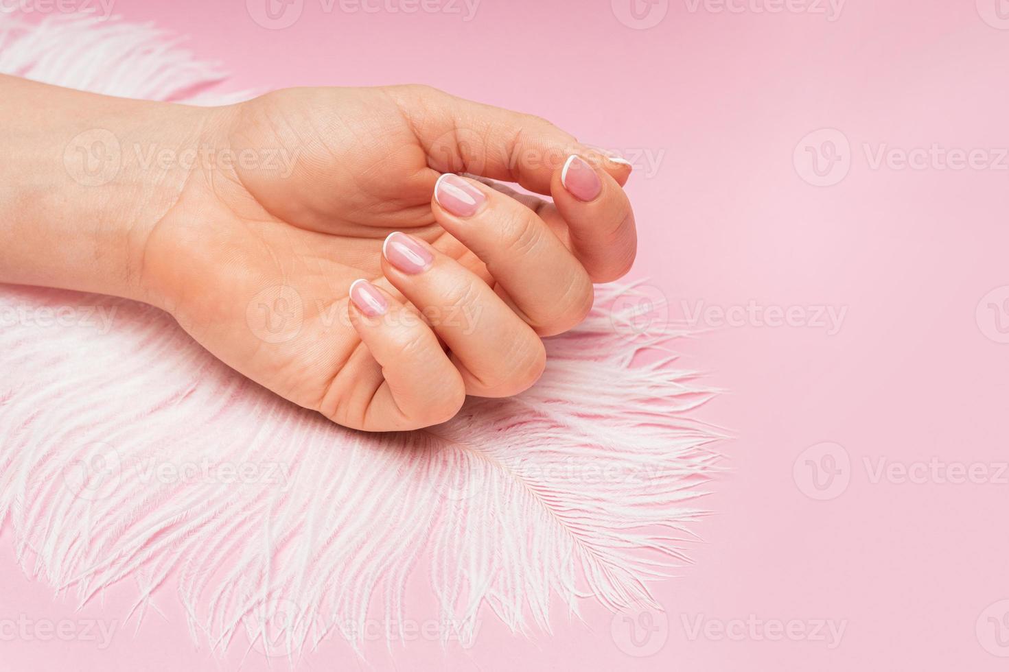 mão feminina com pele lisa e penas de avestruz macias em fundo rosa foto