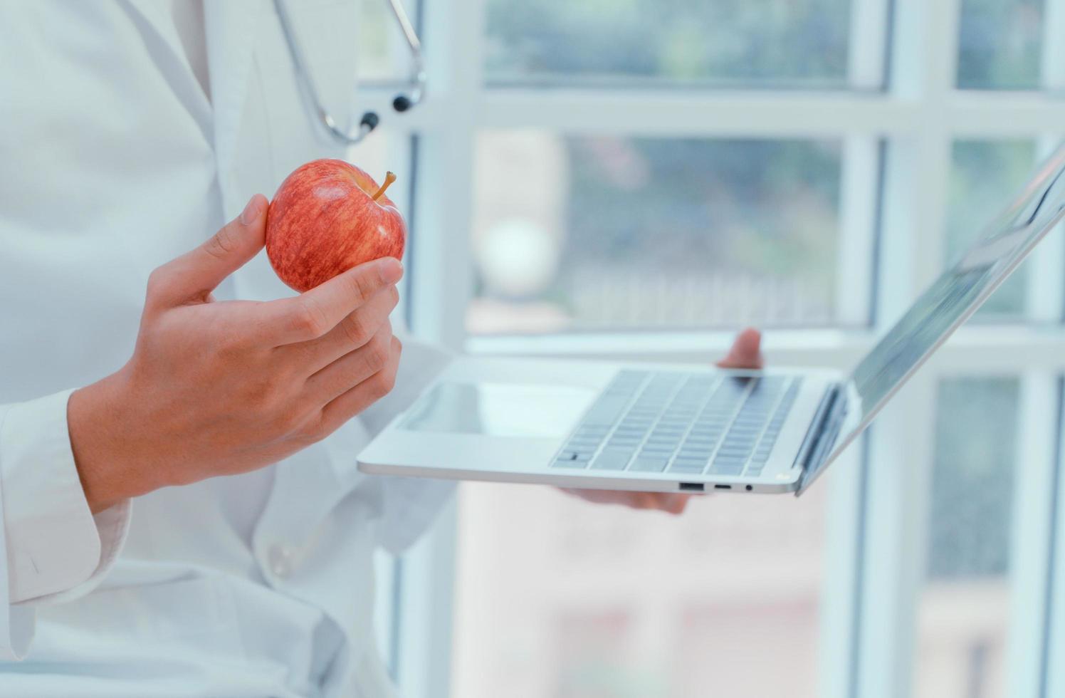 médicos ou nutricionistas seguram maçãs e laptops na clínica para explicar os benefícios das frutas e vegetais. boa saúde começa com você. conceito de comida útil. foto