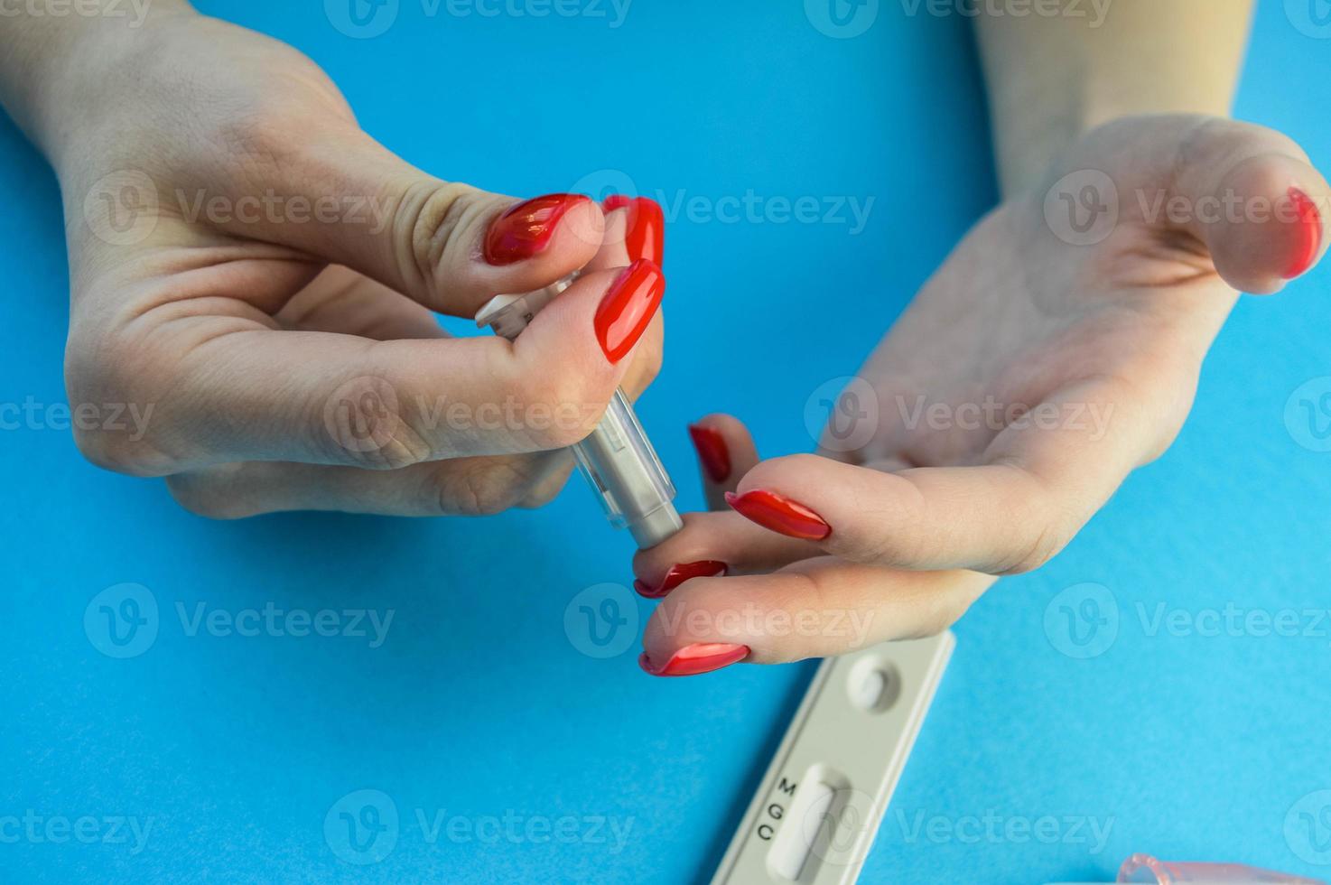 punção de dedo para diagnosticar coronavírus. menina com manicure vermelha faz uma análise por conta própria. menina segurando uma lanceta e pica o dedo com a segunda mão, diagnóstico em casa foto