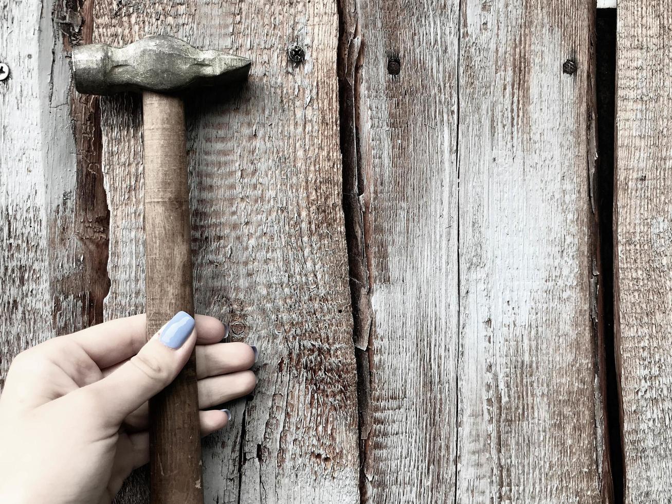 martelo em um cabo de madeira com ponta de metal. menina com manicure azul martelo pregos em uma cerca de madeira. unhas elegantes, manicure na moda. mulher carpinteira foto