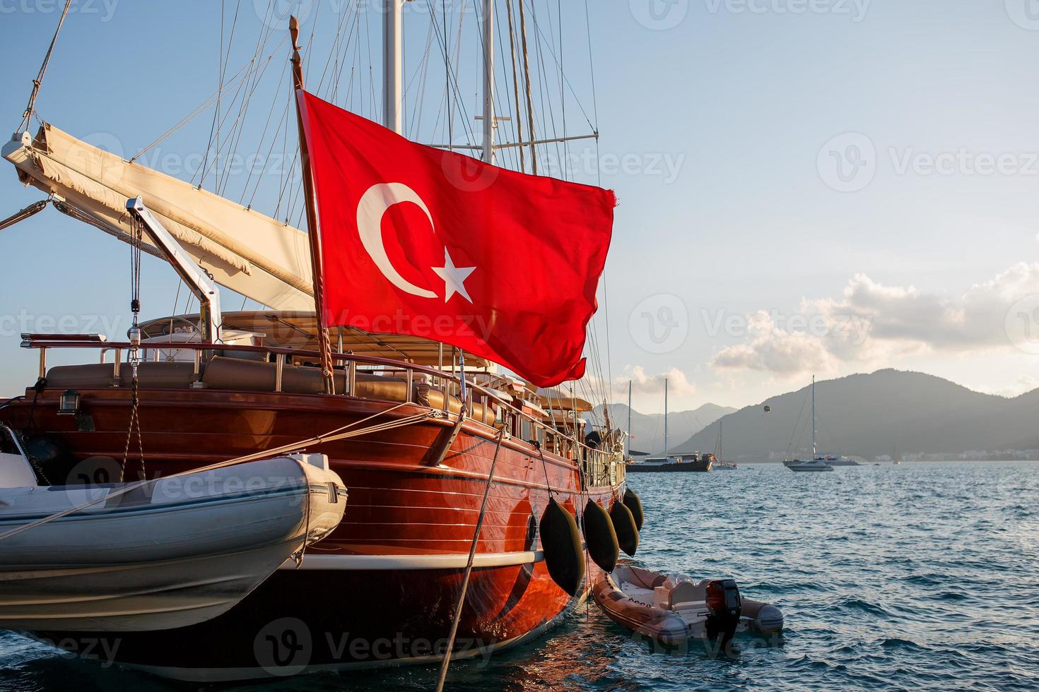 lindo iate de madeira com a grande bandeira da Turquia no cais, tendo como pano de fundo um lindo céu pôr do sol com raios solares foto