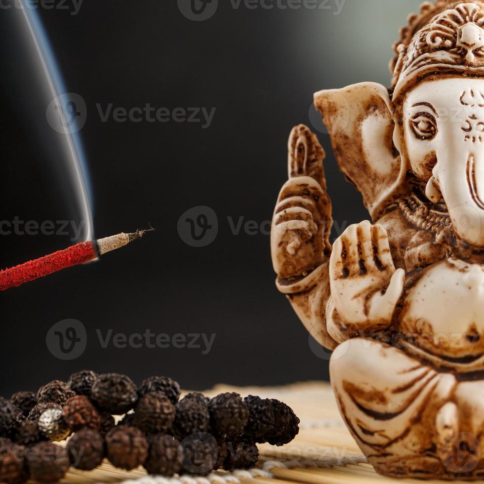 deus hindu ganesh em um fundo preto. estátua rudraksha e rosário em uma mesa de madeira com um bastão de incenso vermelho e fumaça de incenso foto