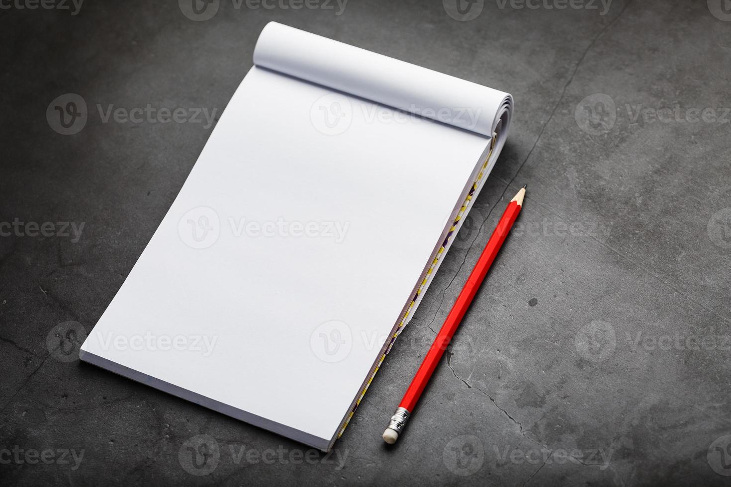 bloco de notas com um lápis vermelho sobre fundo de placa de pedra preta, para educação, registro de objetivos e ações foto