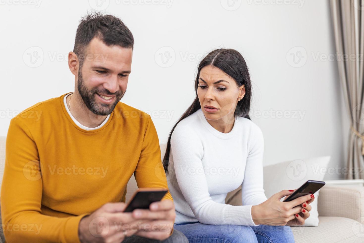 homem sorridente feliz virou as costas para a esposa, lendo a mensagem no telefone de seu amante, mulher preocupada sentada ao lado dele, tentando espiar a tela. conceito de traição e infidelidade foto