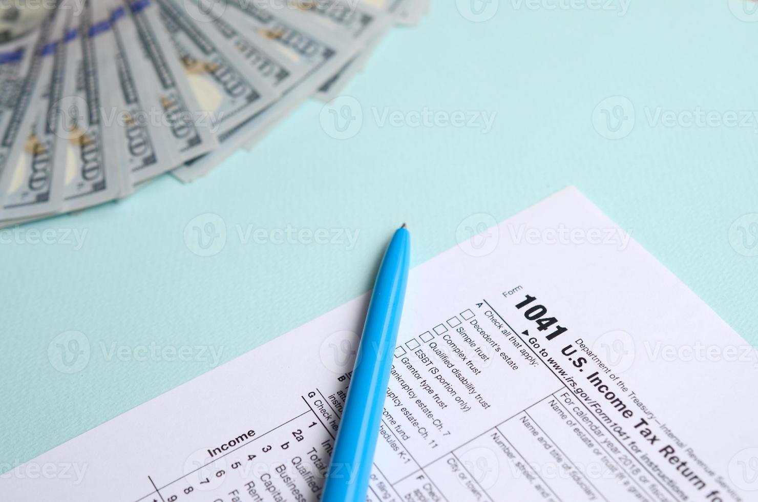 1041 formulário de imposto fica perto de notas de cem dólares e caneta azul sobre um fundo azul claro. nos retorno de imposto de renda para propriedades e fundos foto