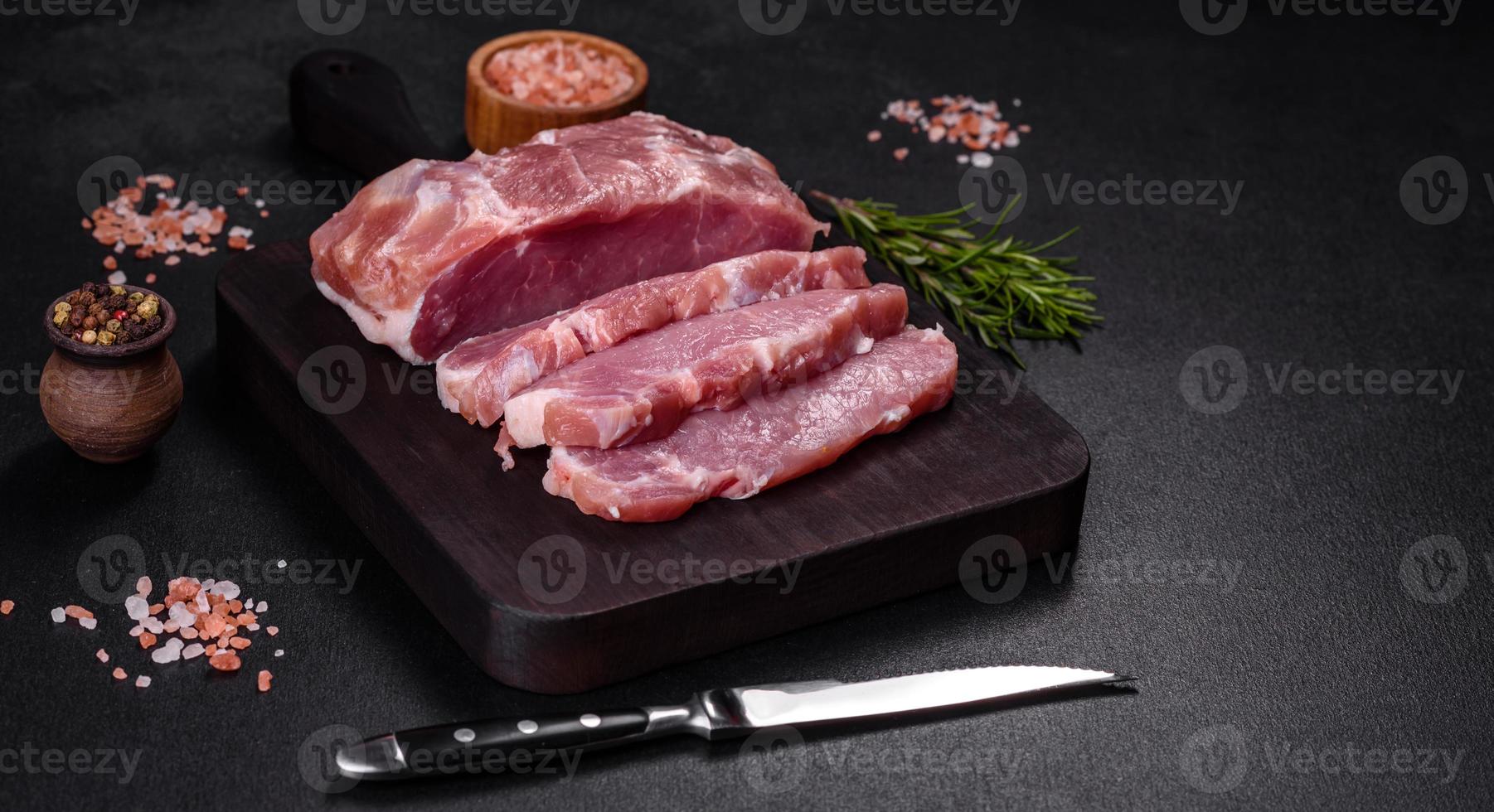 pedaço fresco de carne de porco crua com especiarias, sal e ervas em uma tábua de madeira foto