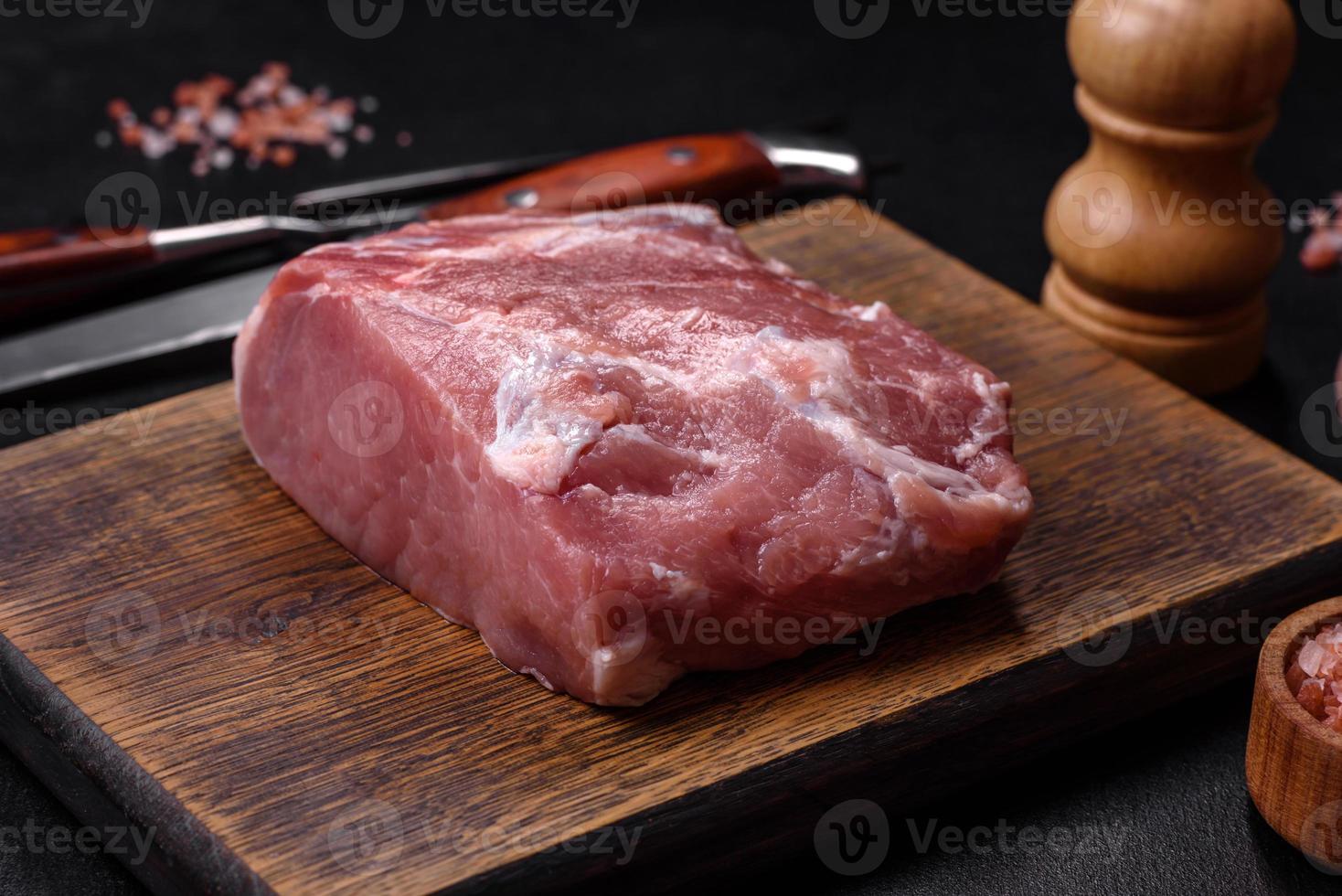 pedaço fresco de carne de porco crua com especiarias, sal e ervas em uma tábua de madeira foto