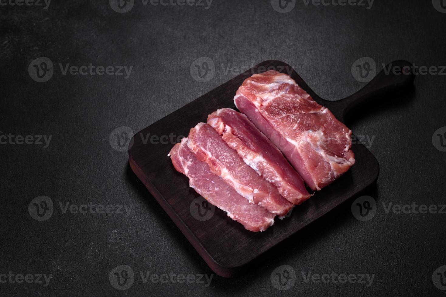 pedaço fresco de carne de porco crua com especiarias, sal e ervas em uma tábua de madeira foto