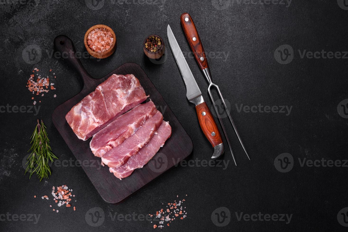 pedaço fresco de carne de porco crua com especiarias, sal e ervas em uma tábua de madeira foto