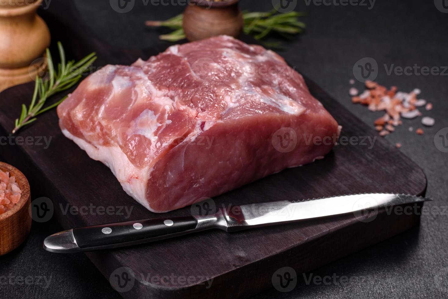 pedaço fresco de carne de porco crua com especiarias, sal e ervas em uma tábua de madeira foto