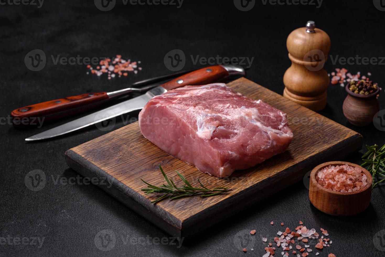 pedaço fresco de carne de porco crua com especiarias, sal e ervas em uma tábua de madeira foto