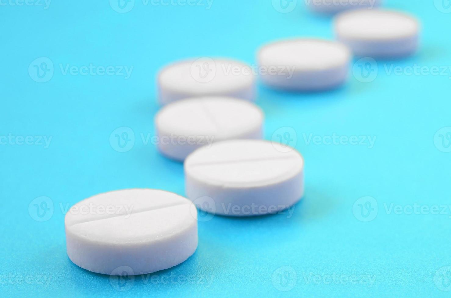 alguns comprimidos brancos repousam sobre uma superfície de fundo azul brilhante. imagem de fundo em tópicos médicos e farmacêuticos foto