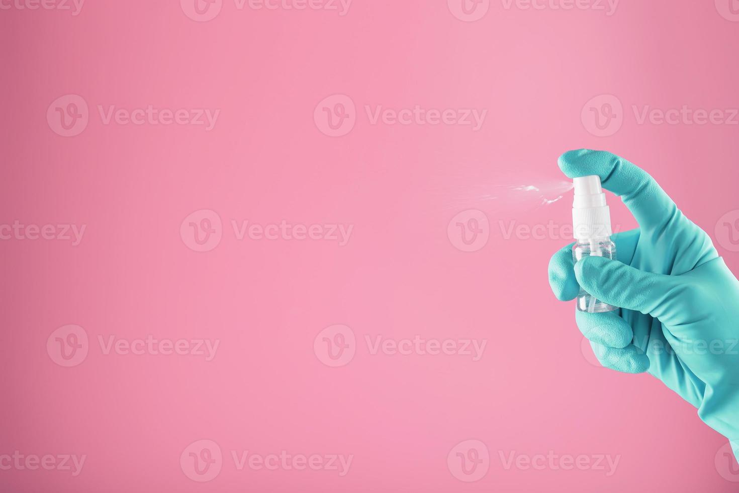 uma mão com luva azul segura um desinfetante em um fundo rosa. tratamento anti-séptico das mãos com desinfetante de bactérias. foto