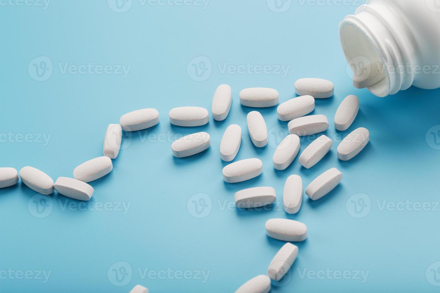 vitaminas e minerais em cápsulas brancas caíram de uma jarra branca sobre fundo azul. foto