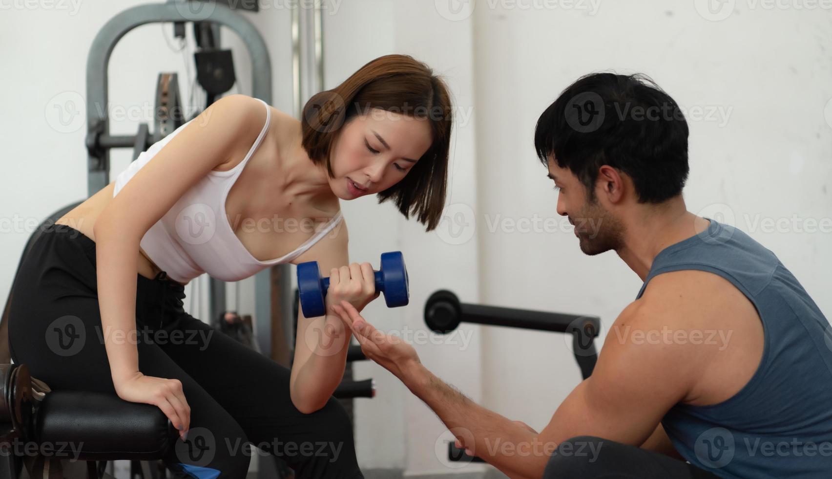 jovem casal se exercitando em uma academia ao levantar pesos, eles se ajudam. conceito de musculação e vida saudável foto