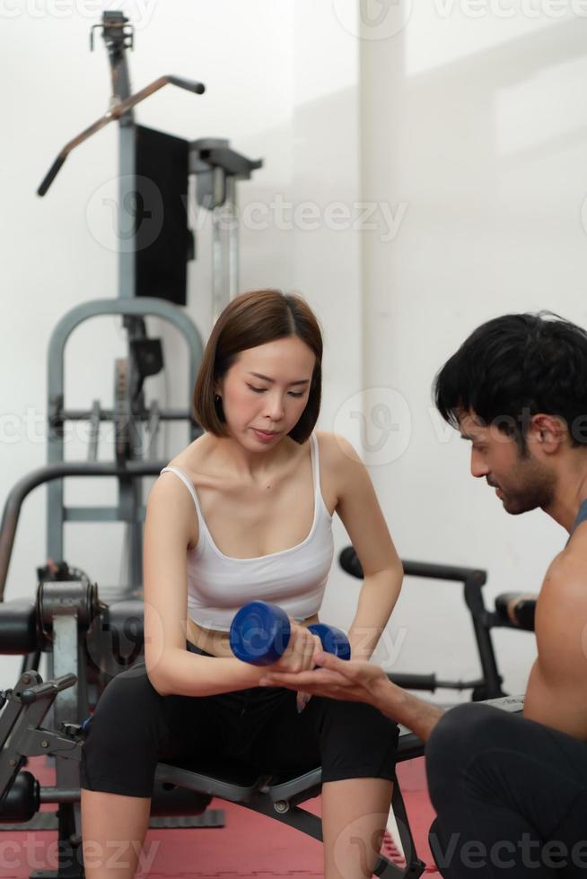 jovem casal se exercitando em uma academia ao levantar pesos, eles se ajudam. conceito de musculação e vida saudável foto