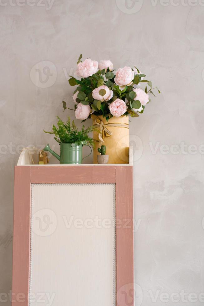 um buquê de peônias artificiais em um vaso, vegetação em um regador no armário do quarto das crianças foto