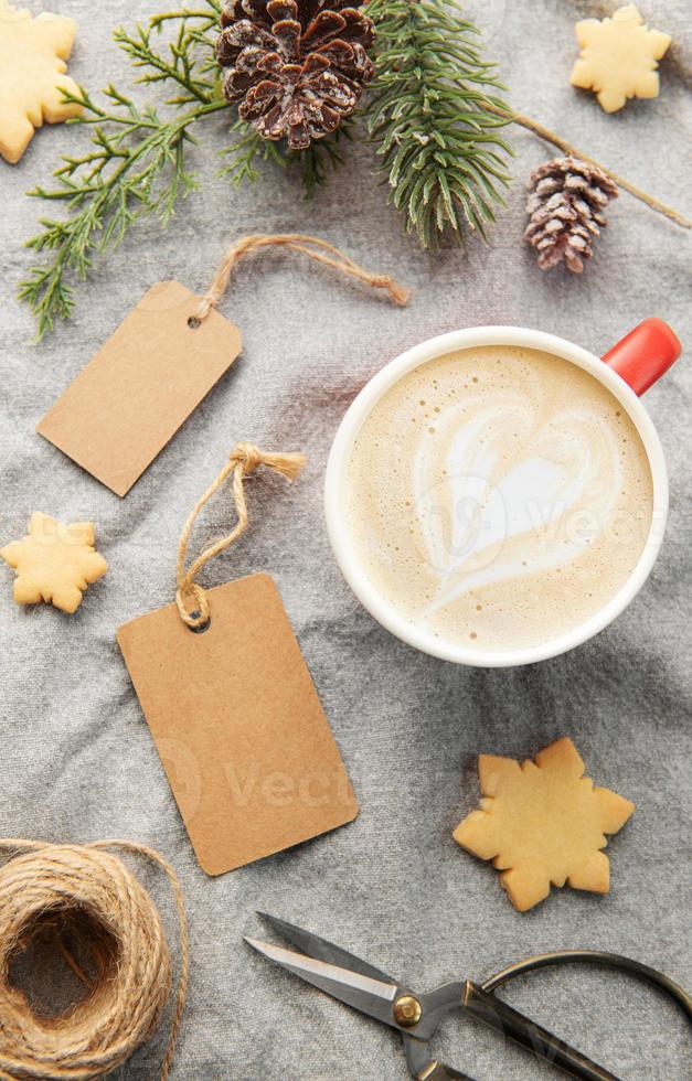 etiquetas de presente em branco com ramo de pinheiro, xícara de café e biscoitos de natal em fundo têxtil. o conceito de preparação para o feriado de natal foto