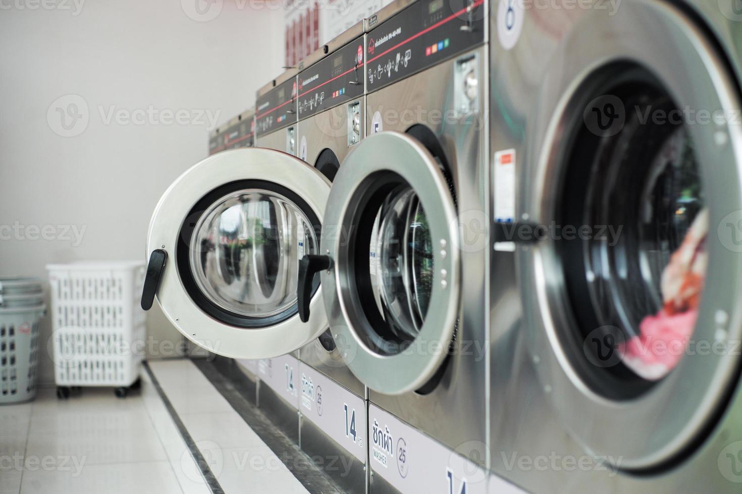 foco seletivo na porta da frente da máquina de lavar com portas fechadas desfocadas em primeiro plano. linha de máquinas de lavar na lavanderia foto