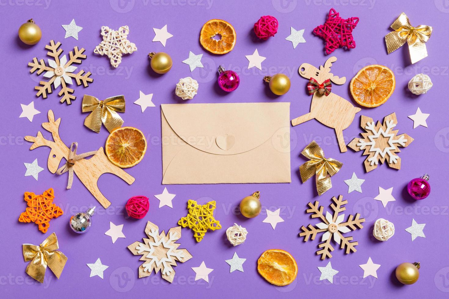 vista superior do envelope de artesanato rodeado de brinquedos de ano novo e decorações em fundo roxo. conceito de tempo de natal foto