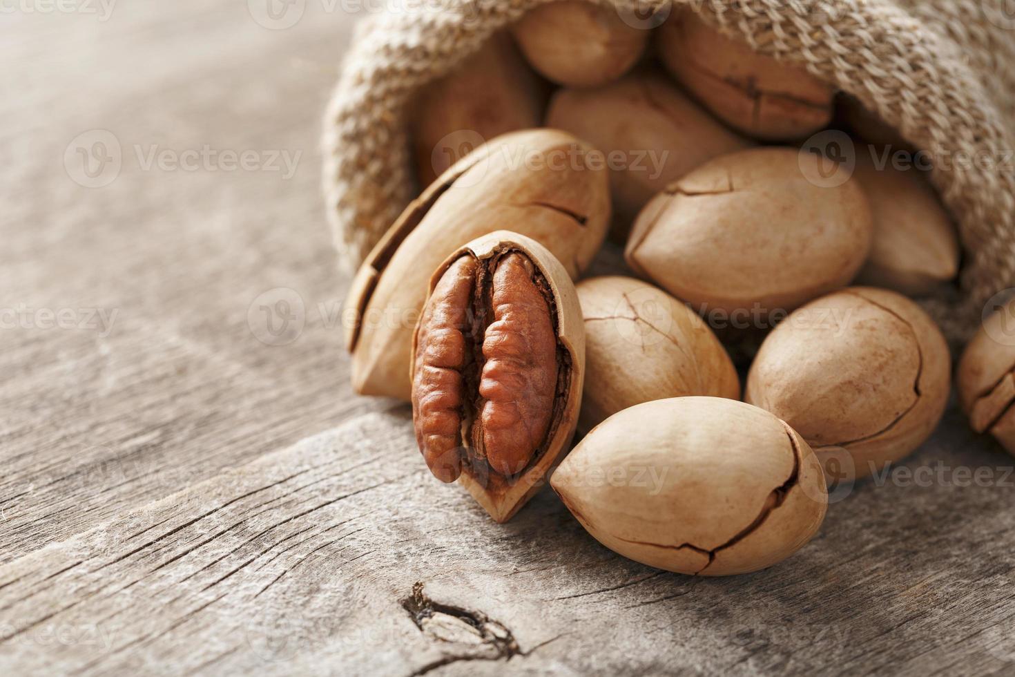 pecans derramam de um saco em uma mesa de madeira, close-up. descascado, em uma casca. foto