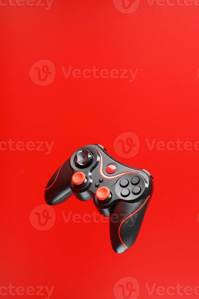 um controlador de jogo joystick preto paira isolado em um fundo vermelho. entretenimento interativo. foto