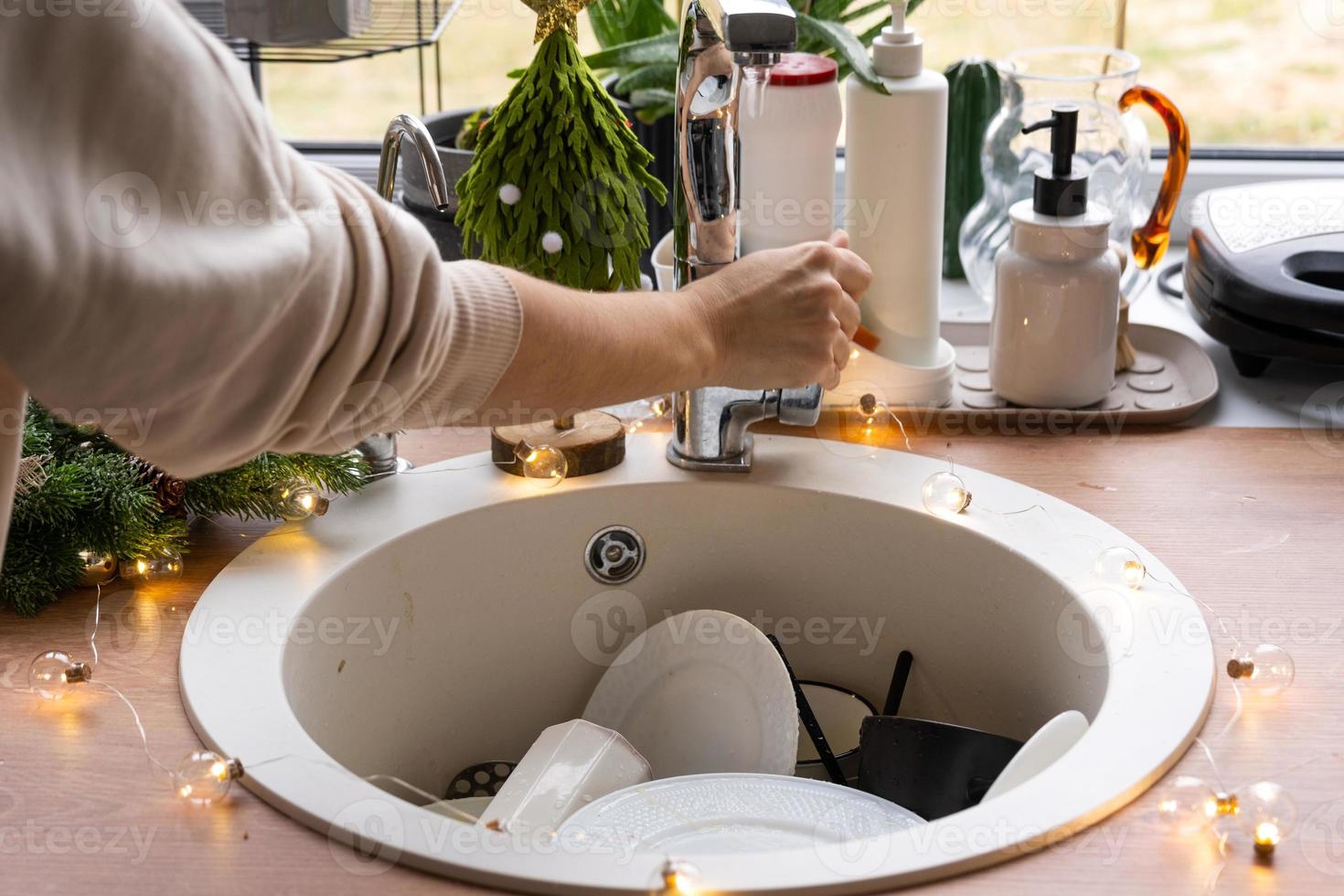 pratos sujos na pia da cozinha com guirlandas, um feriado depois de uma festa de natal. bagunça depois dos convidados para o ano novo, limpeza de cozinha, detergente, serviços de limpeza foto