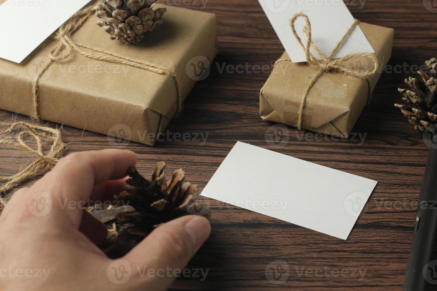 mãos masculinas embrulhando presentes de ano novo e escrevendo cartões em uma mesa de madeira marrom. foto