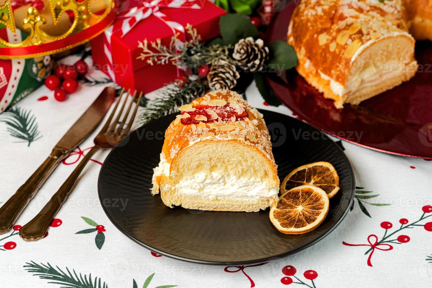 porção de roscon de reyes com creme e enfeites de natal em um prato preto. conceito do dia dos reis bolo espanhol de três reis sobremesa espanhola típica para o natal foto