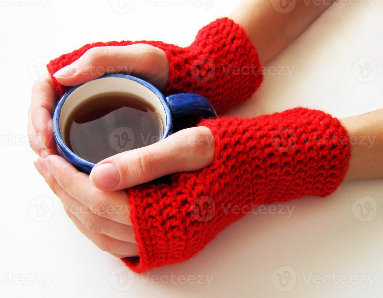 mãos femininas em luvas vermelhas estão segurando um copo de bebida quente. mulher segura uma xícara de café foto