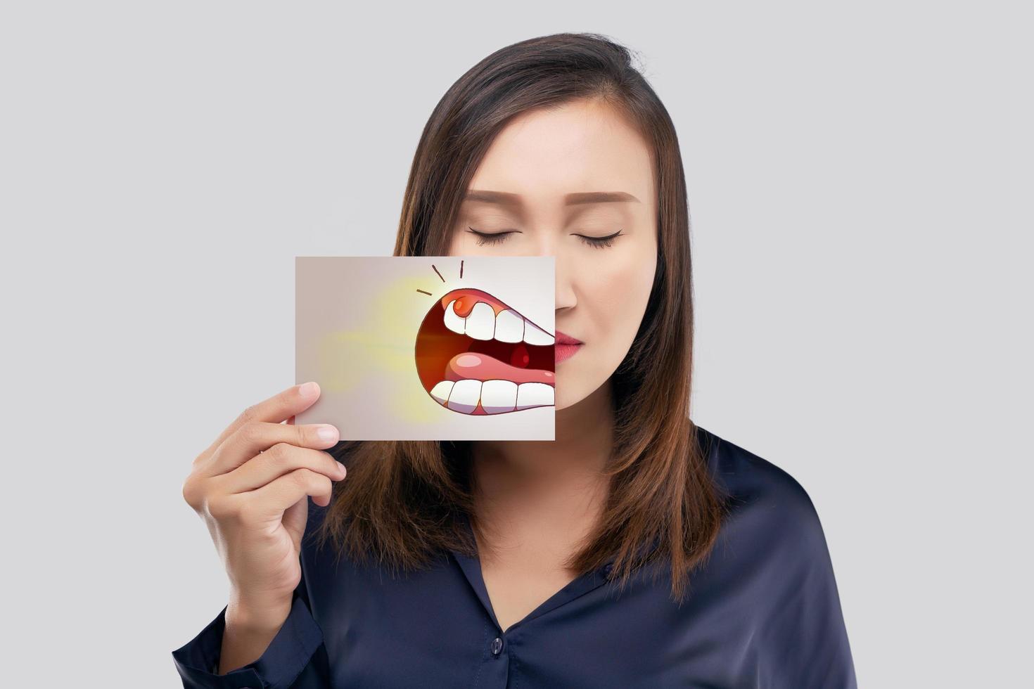 mulher asiática segurando um papel com a imagem de desenho animado periodontal e gengivite de sua boca contra o fundo cinza, dente cariado, o conceito com gengivas e dentes de saúde foto