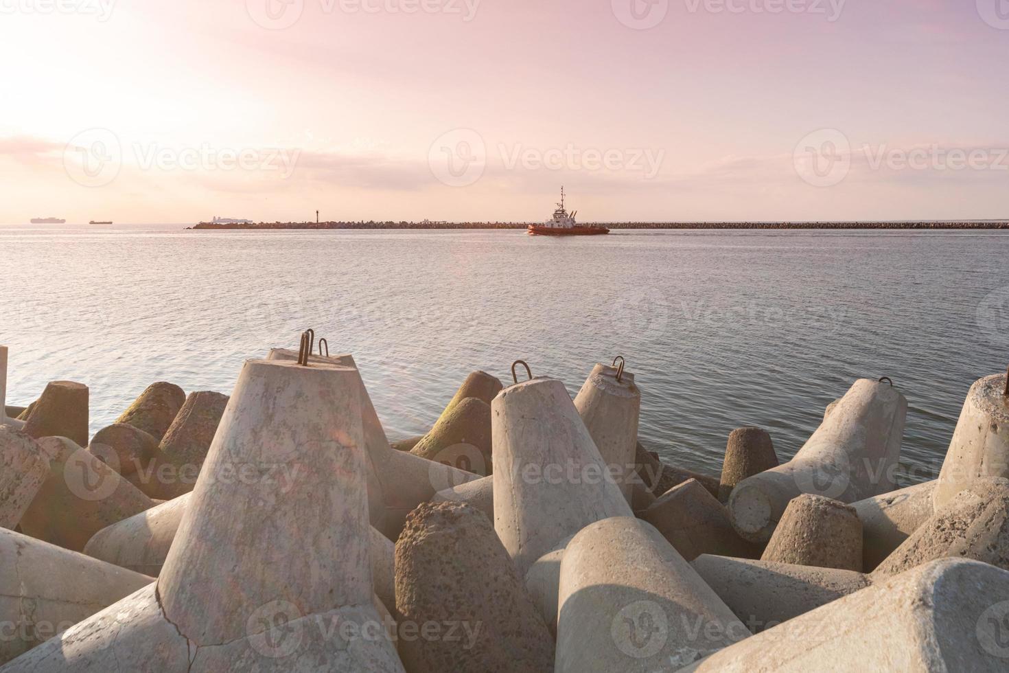 navio-rebocador vai em alto mar para rebocar cargueiro para o porto. belo pôr do sol sobre o cais. quebra-mares tetrápodes no porto. foto