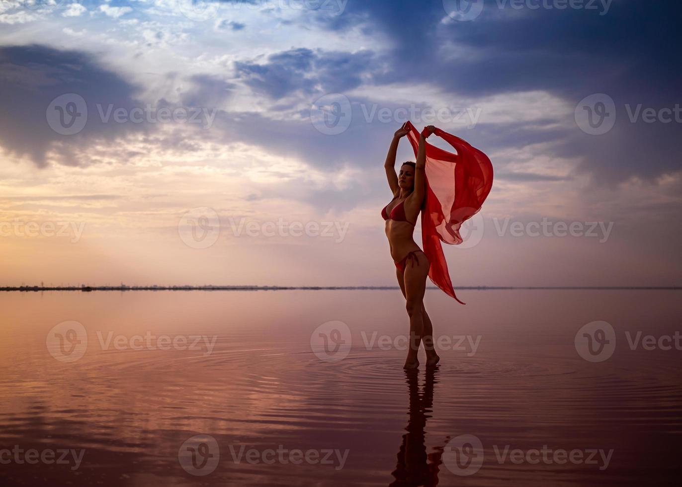 silhueta de uma garota em um maiô vermelho na praia. tecido vermelho se desenvolve em suas mãos. foto