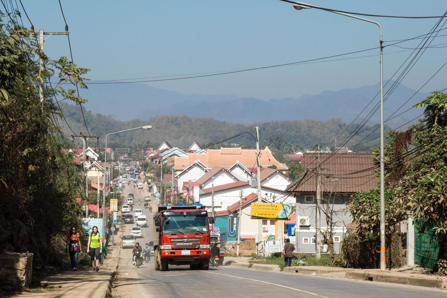 luang prabang, laos - 23 de janeiro de 2018. vista na rua movimentada com transporte diferente, edifícios residenciais, turistas e população local e com montanhas no fundo. foto