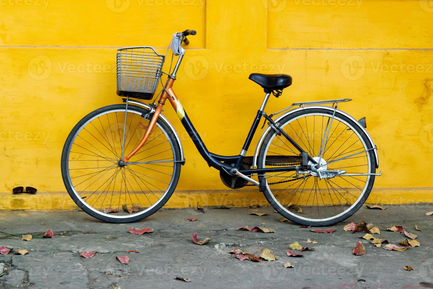 bicicleta velha em um fundo de parede amarela pintada brilhante e folhas de outono em uma rua. foto