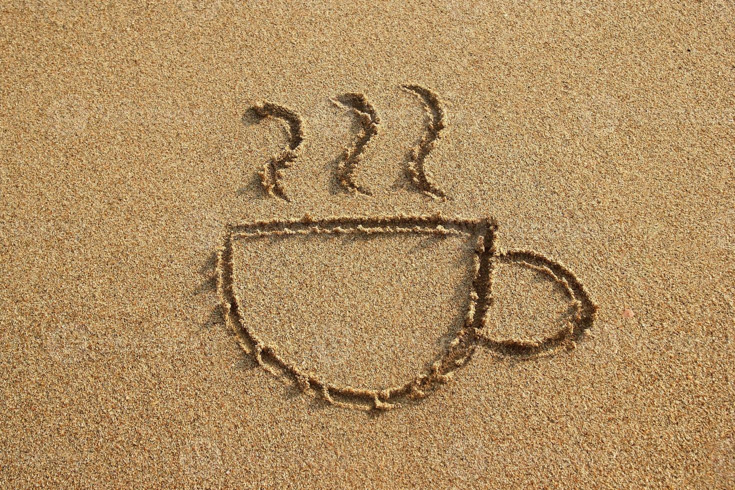 xícara de café é desenhada em uma praia de areia em um pôr do sol, vista superior. foto