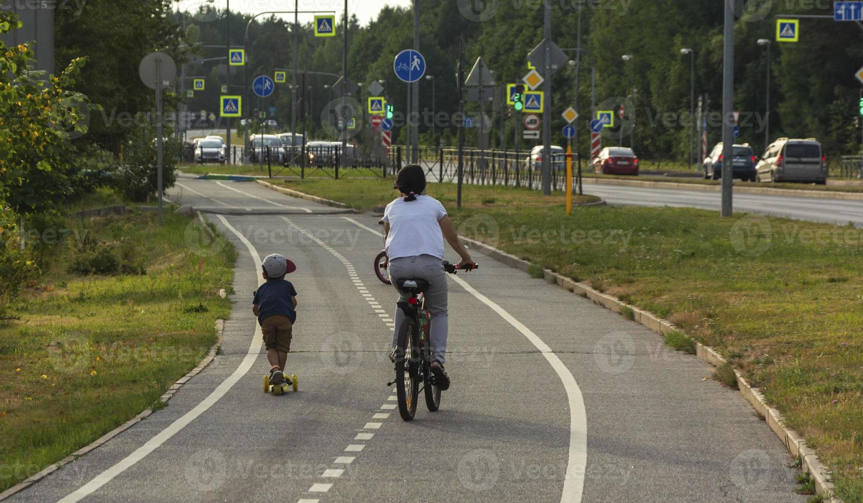 mãe e filho andam de bicicleta e scooter em uma ciclovia na cidade, passeio de bicicleta em família, recreação ativa, vida na cidade foto