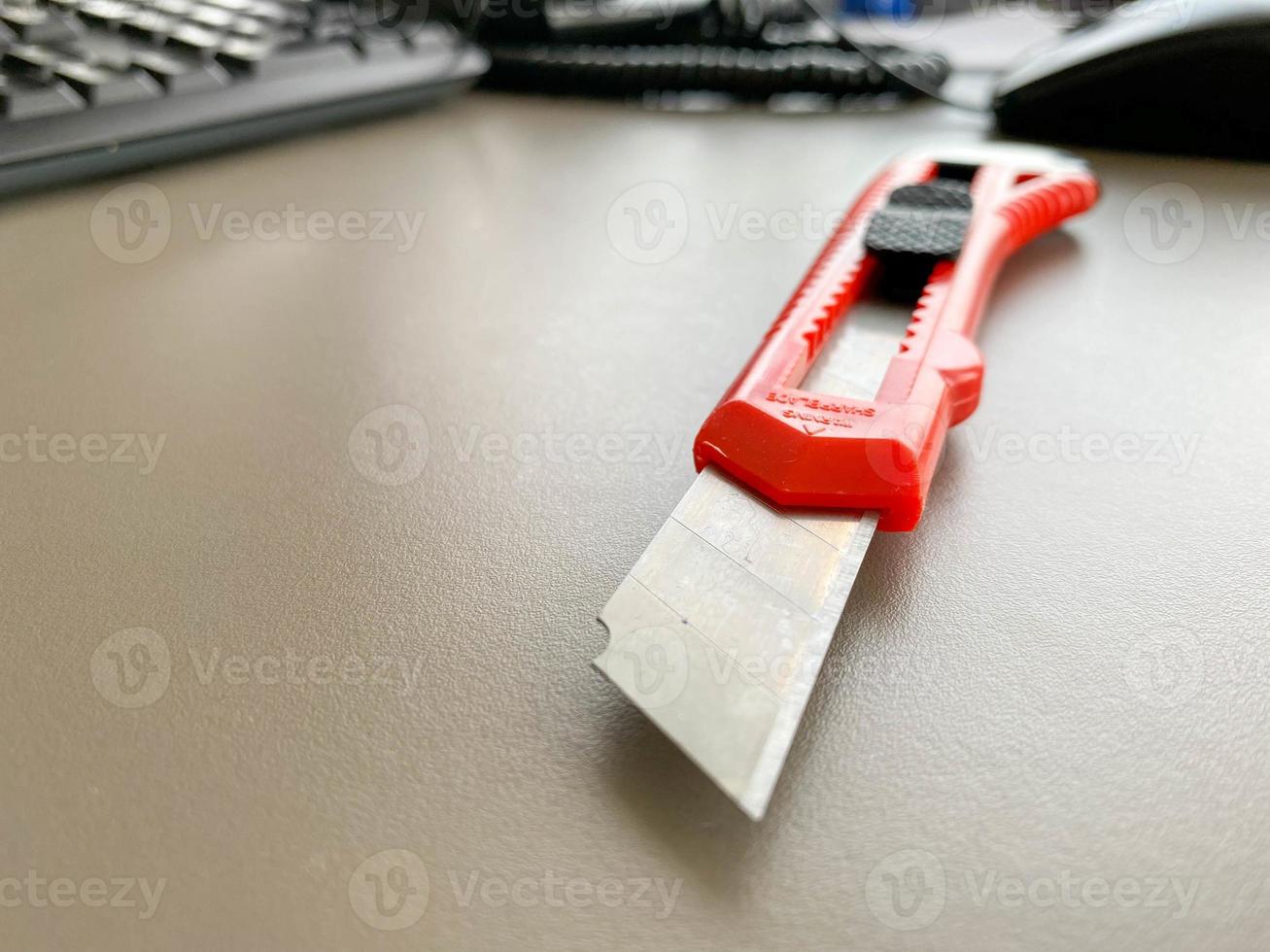 faca de papelaria de escritório vermelha afiada com uma lâmina de corte de papel em uma mesa de escritório. trabalho de negócios foto