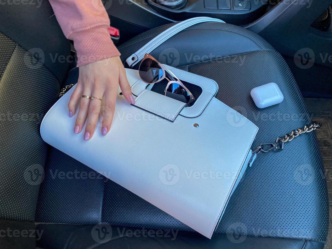 bolsa de couro elegante feminina branca bonita e óculos de sol com fones de ouvido sem fio e mão feminina no carro foto