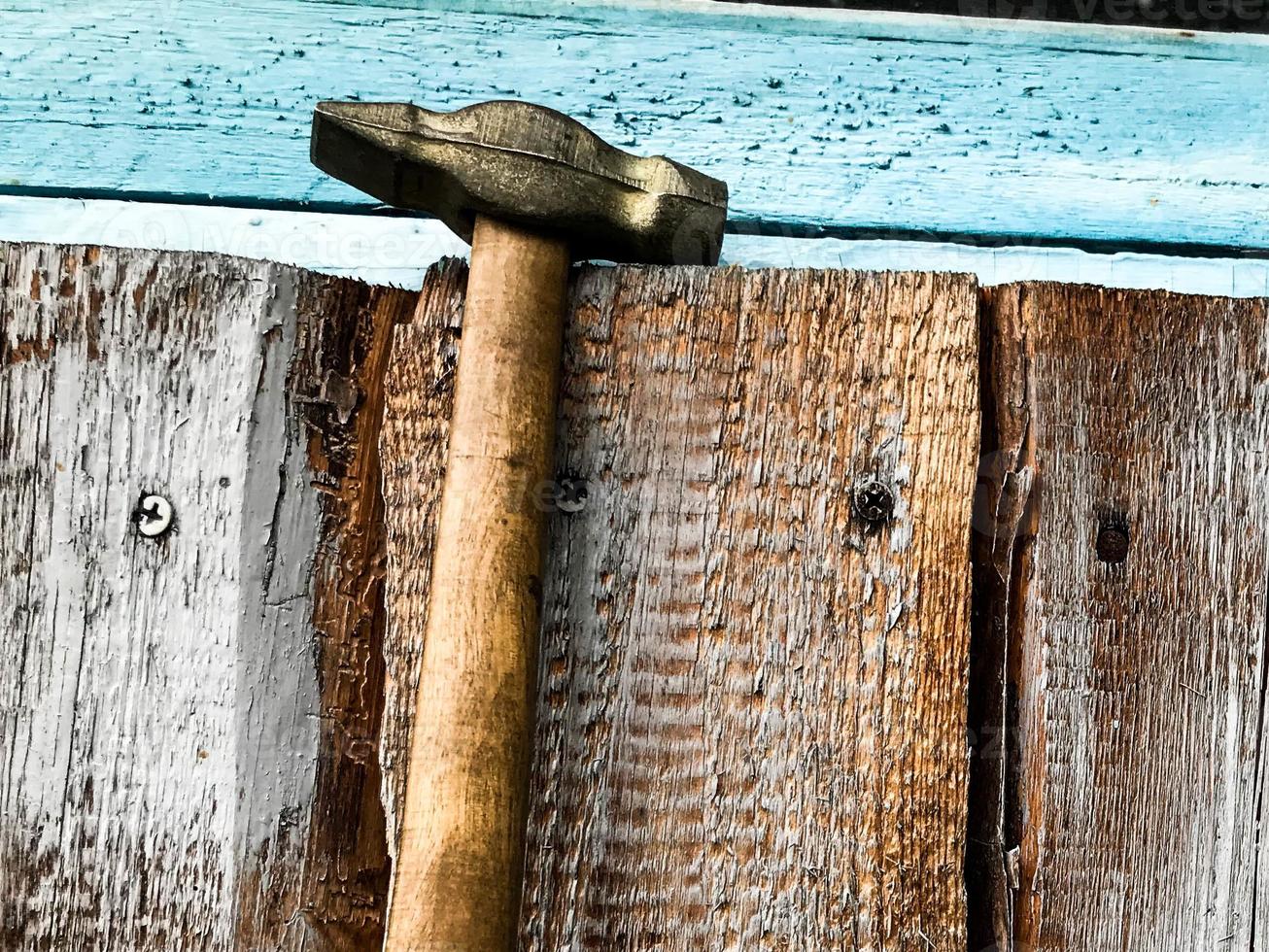 martelo em um cabo de madeira com ponta de metal. o martelo está pendurado em uma cerca de madeira, manchada de tinta azul. ferramentas para construir e fazer uma cerca, casa. martelando em pregos foto