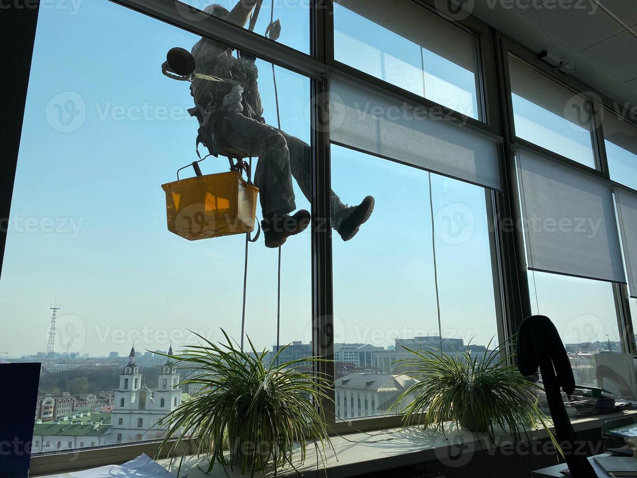 janelas limpas do alpinista do lado de fora do prédio lavando o vidro da fachada de um prédio de vários andares foto